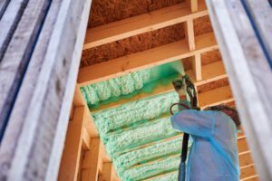 Worker spraying polyurethane foam for insulating wooden frame house